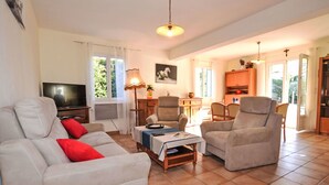 Un salon comprenant un canapé, des fauteuils, une table basse, un téléviseur et un coin repas avec une table et des chaises.