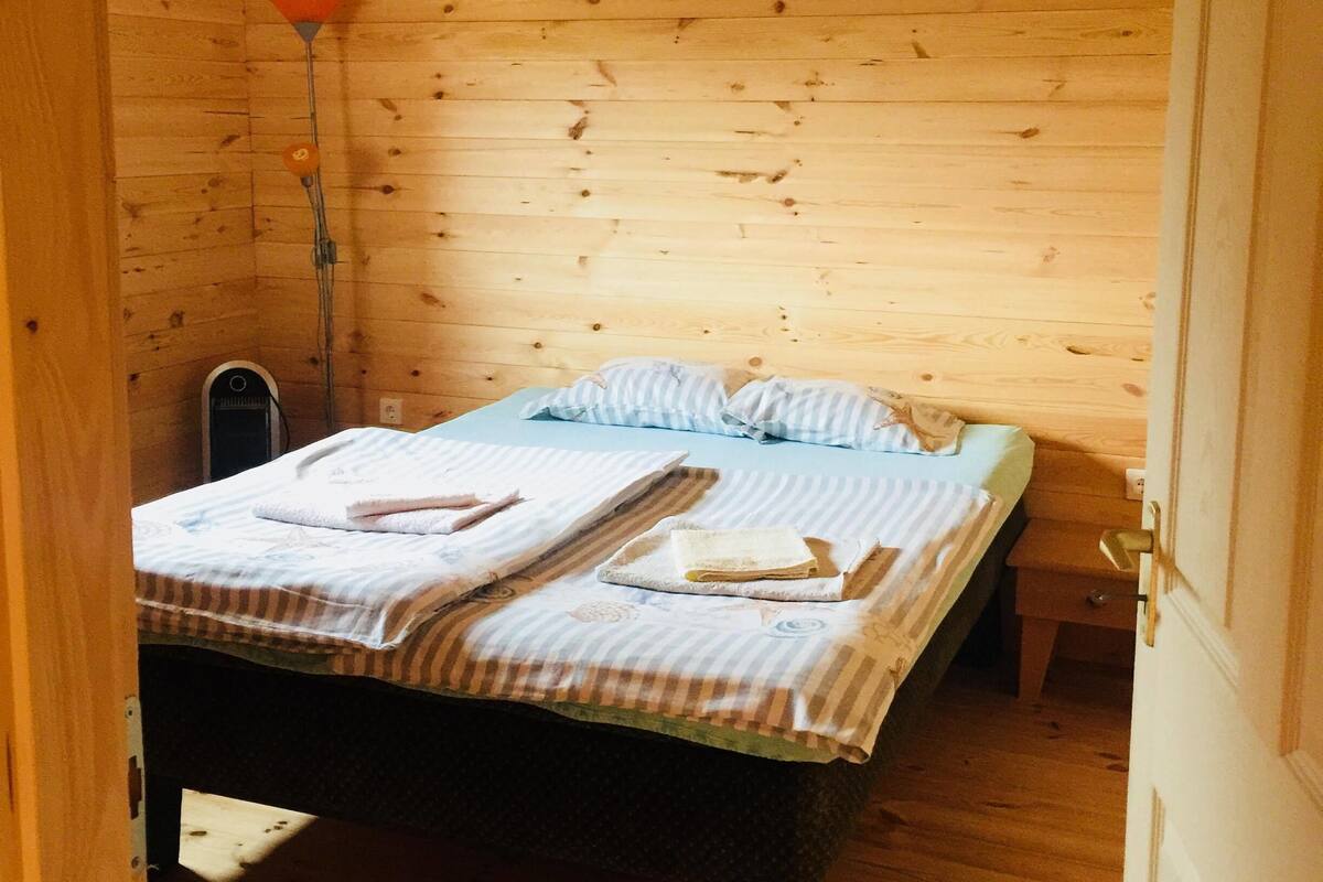 A wooden cabin room with a bed, a bedside table, and a lamp.