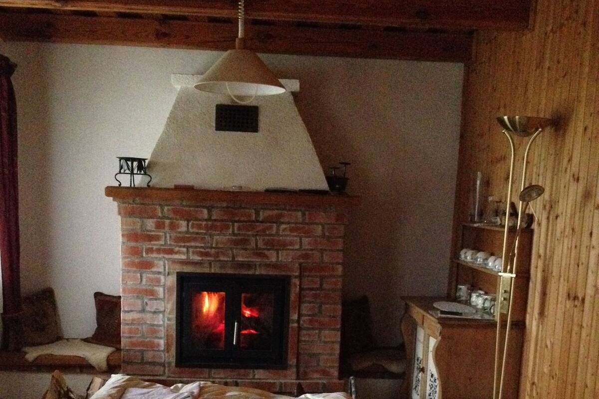 A cozy room with a brick fireplace, a bed with a striped blanket, and a wooden ceiling.