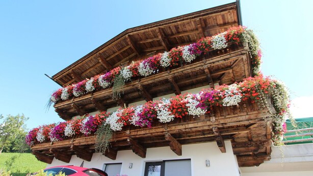 A multi-story building with wooden balconies adorned with colorful flowers. - Beautiful apartment for 6 people with WIFI, TV, patio and panoramic view (Mitterdorf)
