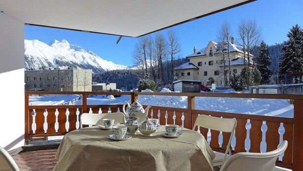 A balcony with a table set for tea, overlooking a snowy mountain landscape and a building. - Nice apartment for 6 guests with WIFI, TV, balcony, pets allowed and panoramic view (Celerina)