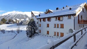 A snow-covered building with multiple windows and a balcony, surrounded by a snowy landscape and mountains in the background. - Nice apartment for 6 guests with WIFI, TV, balcony, pets allowed and panoramic view (Celerina)