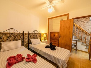 Une chambre d’hôtel avec deux lits simples, une armoire en bois, une petite table avec une lampe et un escalier menant à l’étage supérieur.