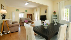Ein Wohnzimmer mit einer Couch, einem Esstisch mit Stühlen, einem Fernseher und einem Schrank.