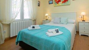 Ein ordentlich eingerichtetes Schlafzimmer mit einem Bett, zwei Nachttischen, einem Fenster mit Vorhängen und Wandbildern.