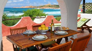 Mesa dispuesta con platos, vasos, limones y una botella, con vistas a la costa y un cielo despejado.