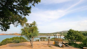 Un parque infantil con columpios y una estructura de madera, rodeado de árboles y vistas al mar.