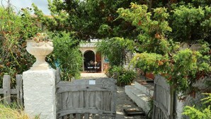 Una rústica puerta de madera que da a un sendero de piedra, rodeada de exuberante vegetación y una pequeña entrada arqueada a un edificio.