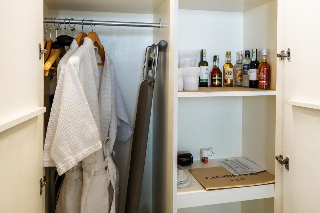 A closet with hanging robes and a shelf with bottles.
