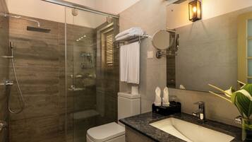 A modern bathroom with a glass-enclosed shower, a white toilet, a marble sink, and a large mirror.