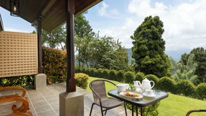 A patio with a table set for tea, surrounded by lush greenery and a view of the landscape. - Simpson's Forest Hotel (Wattegama)