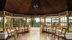 A gazebo with four wooden chairs and a chandelier, large windows offering a view of the mountains. - Simpson's Forest Hotel (Wattegama)