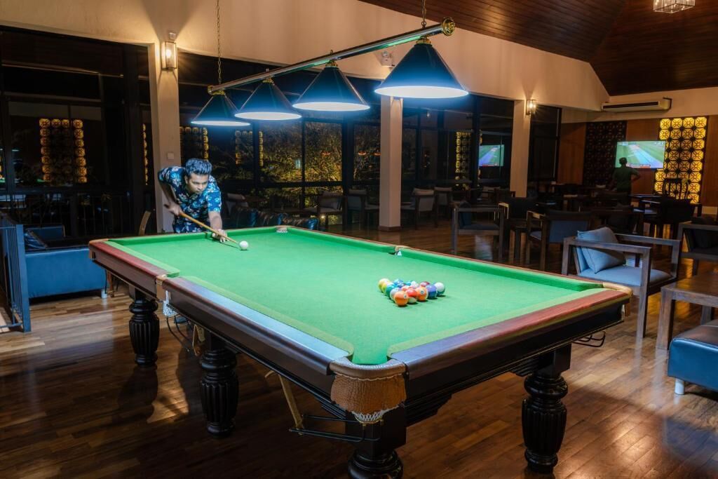 A pool table in a room with wooden flooring and large windows.