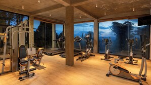 A gym with various exercise equipment, large windows, and a concrete ceiling. - Simpson's Forest Hotel (Wattegama)
