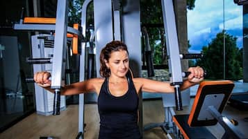 Una mujer haciendo ejercicio en una máquina en un gimnasio con varios equipos y un ventanal grande al fondo.