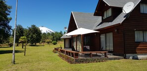 A wooden cabin with a porch, a satellite dish, and a view of a snow-capped mountain. - Parque Los Arrayanes & Salon de Eventos (Villarrica)