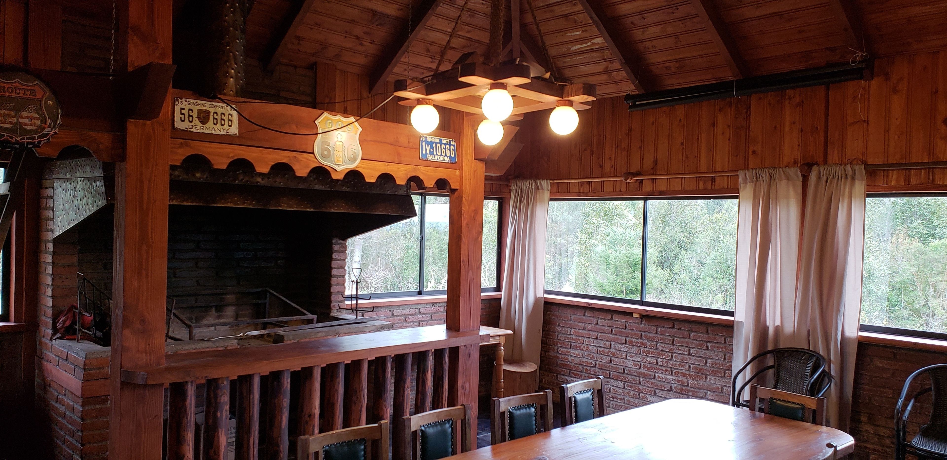Un intérieur rustique avec des éléments en bois, une cheminée en briques, des poutres apparentes et de grandes fenêtres agrémentées de rideaux.