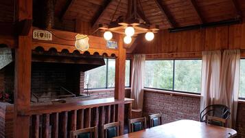 Un intérieur rustique avec des éléments en bois, une cheminée en briques, des poutres apparentes et de grandes fenêtres agrémentées de rideaux.