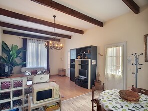 A living room with a sofa, a dining table with a basket, a television, a bookshelf, and a chandelier.