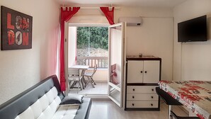 Habitación con cama, televisión, mesa y ventana con vista a la vegetación.