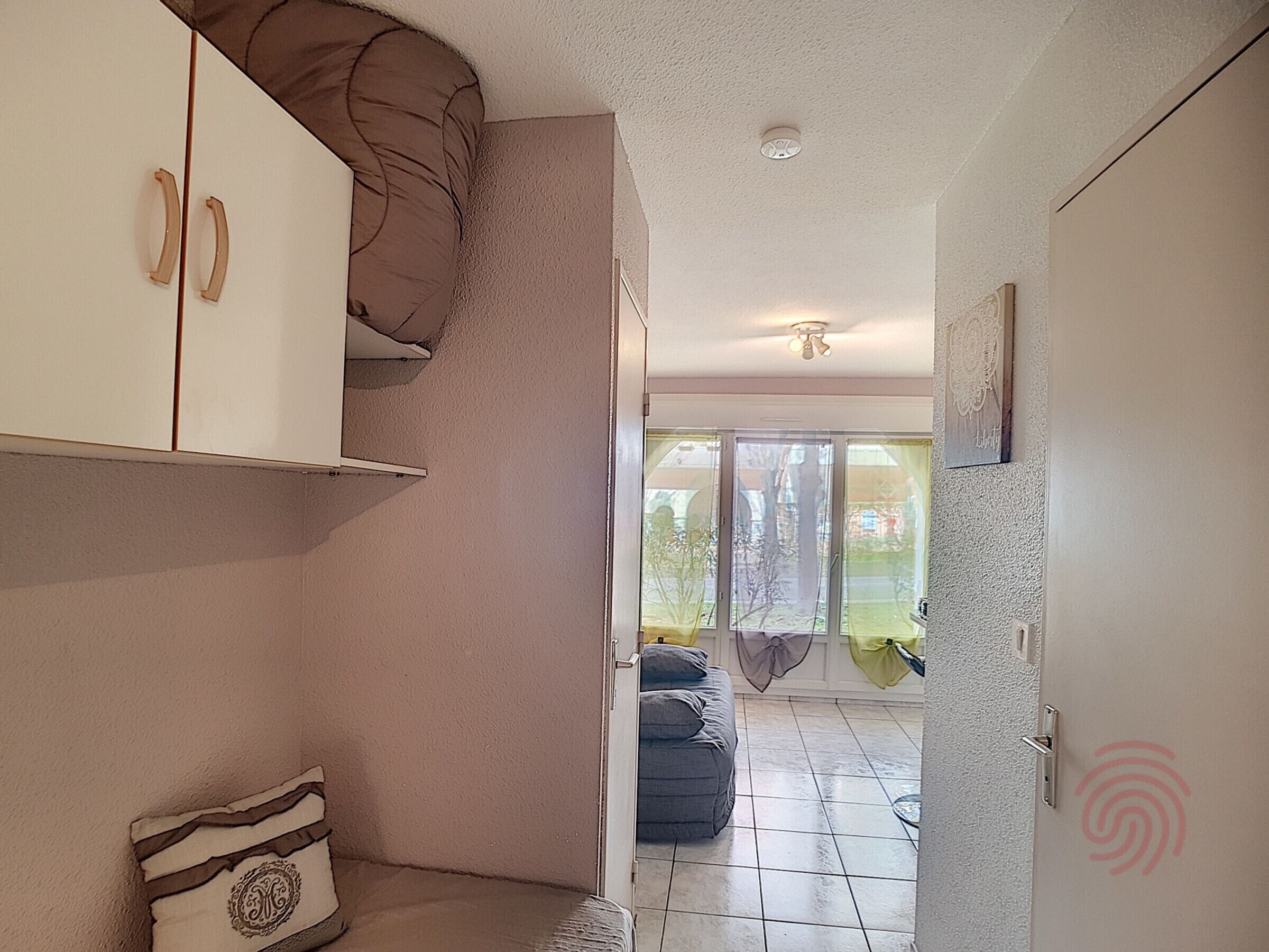 Una habitación con un sofá, un armario, un ventanal corredero que da a un espacio exterior y un ventilador de techo.