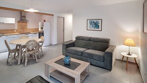 A compact living space with a kitchenette, a grey sofa, a dining area with wicker chairs, and a coffee table with a vase. - Cozy F2 Apartment, A/C, Terrace, Near Thermes & Park, Pet-Friendly, Lamalou-les-Bains (Lamalou-les-Bains)