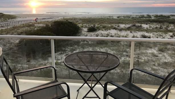 A balcony with a table and chairs overlooking a beach at sunset. - Best Beachfront - Expansive OCEAN VIEWS Perfect location! 2 decks & large patio (Ocean City)