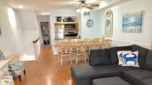 A modern living room with a grey sectional sofa, a patterned armchair, and a dining area with wooden chairs and a table. - Best Beachfront - Expansive OCEAN VIEWS Perfect location! 2 decks & large patio (Ocean City)