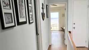 A hallway with framed pictures on the wall, a wooden floor, and a view of the beach through an open door. - Best Beachfront - Expansive OCEAN VIEWS Perfect location! 2 decks & large patio (Ocean City)