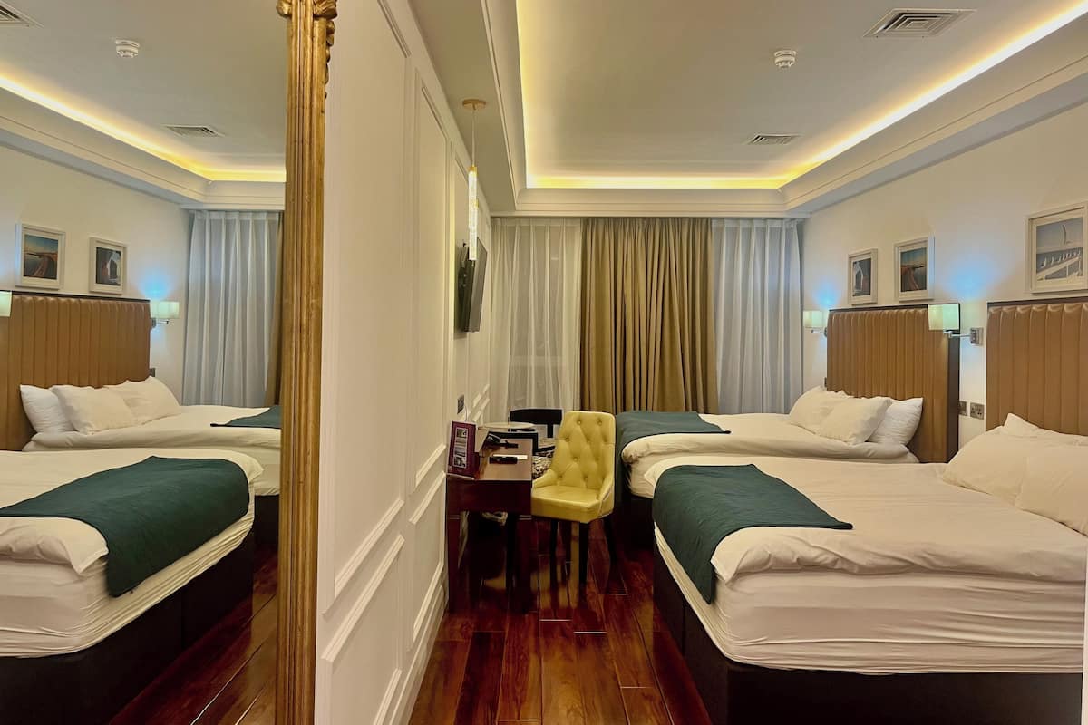 Quarto de hotel com duas camas, uma escrivaninha, uma cadeira e uma televisão.
