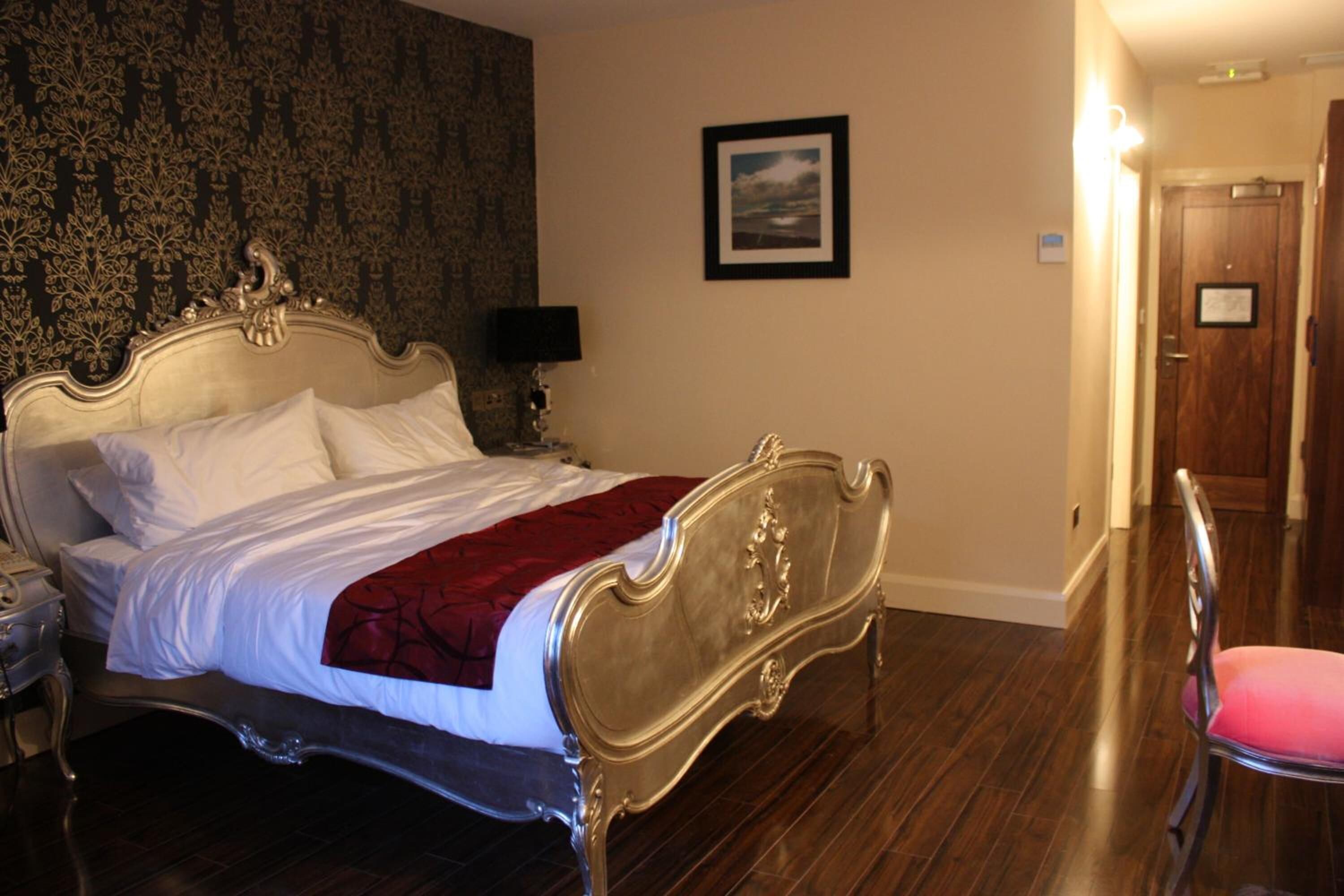 A hotel room with a classic four-poster bed, a wooden floor, a framed picture on the wall, and a door leading to another room.