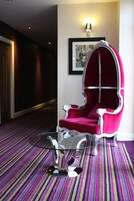 Una habitación de hotel moderna con alfombra a rayas, una mesa de centro de vidrio transparente y un sillón tapizado en rojo.