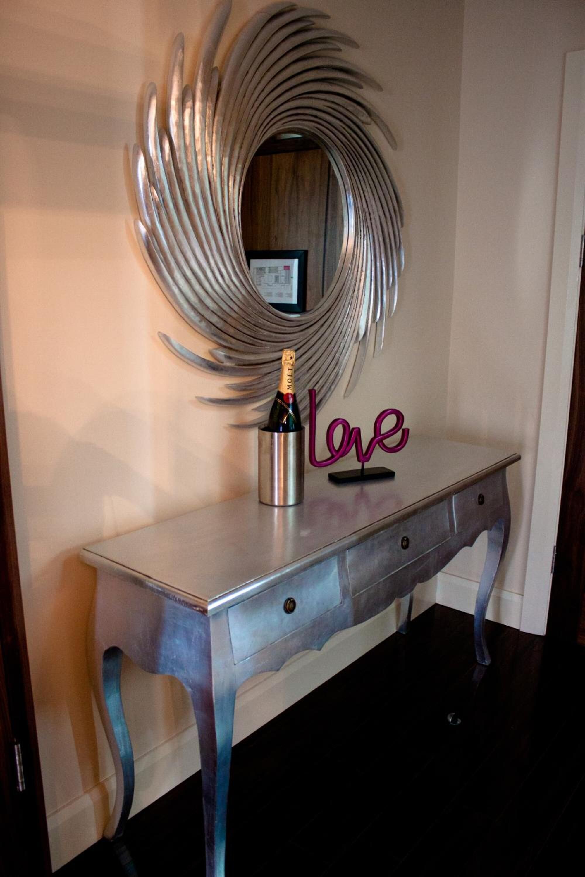 Una obra de arte abstracta de metal sobre un aparador metálico pintado, con una botella de champán y un letrero de neón que dice "love".