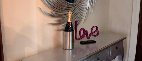 Una obra de arte abstracta de metal sobre un aparador metálico pintado, con una botella de champán y un letrero de neón que dice "love".