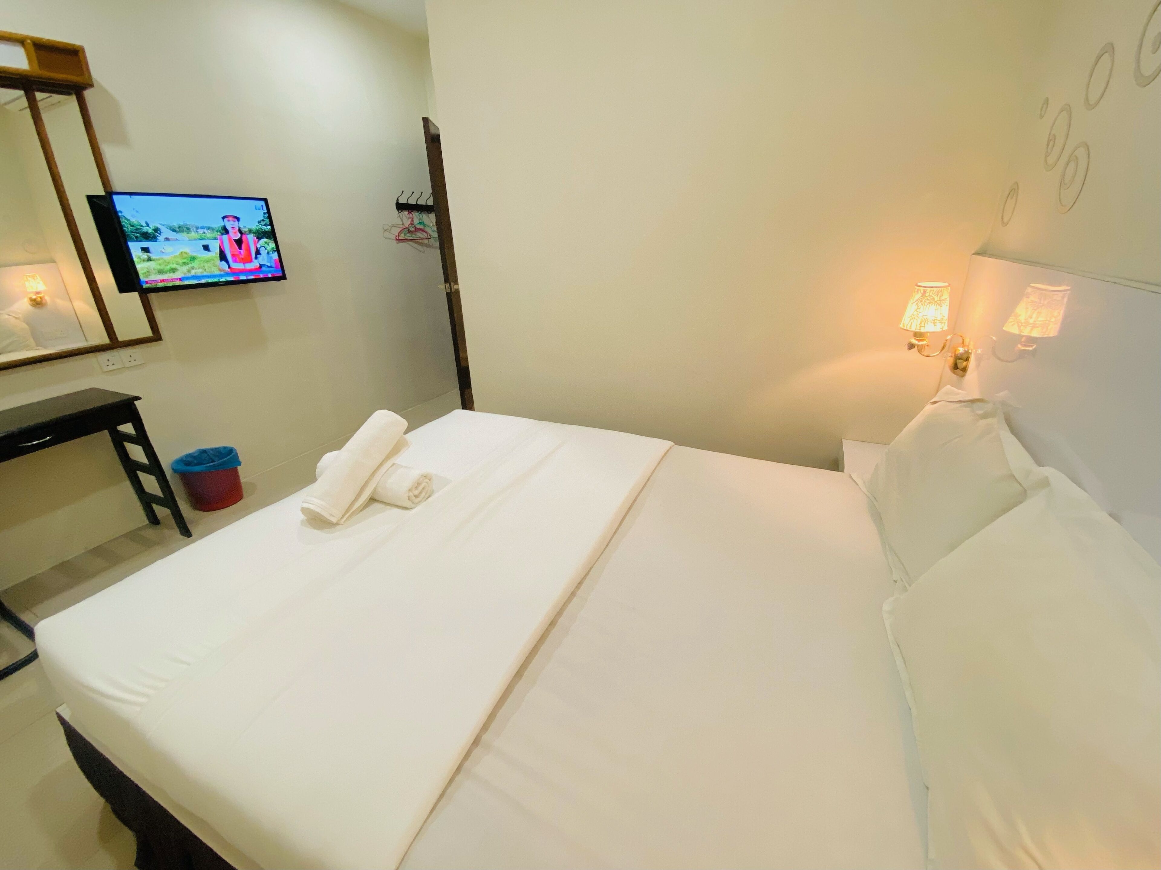 Una habitación de hotel con cama, escritorio, televisor, lámpara de pared y espejo.