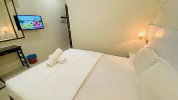 Una habitación de hotel con cama, escritorio, televisor, lámpara de pared y espejo.