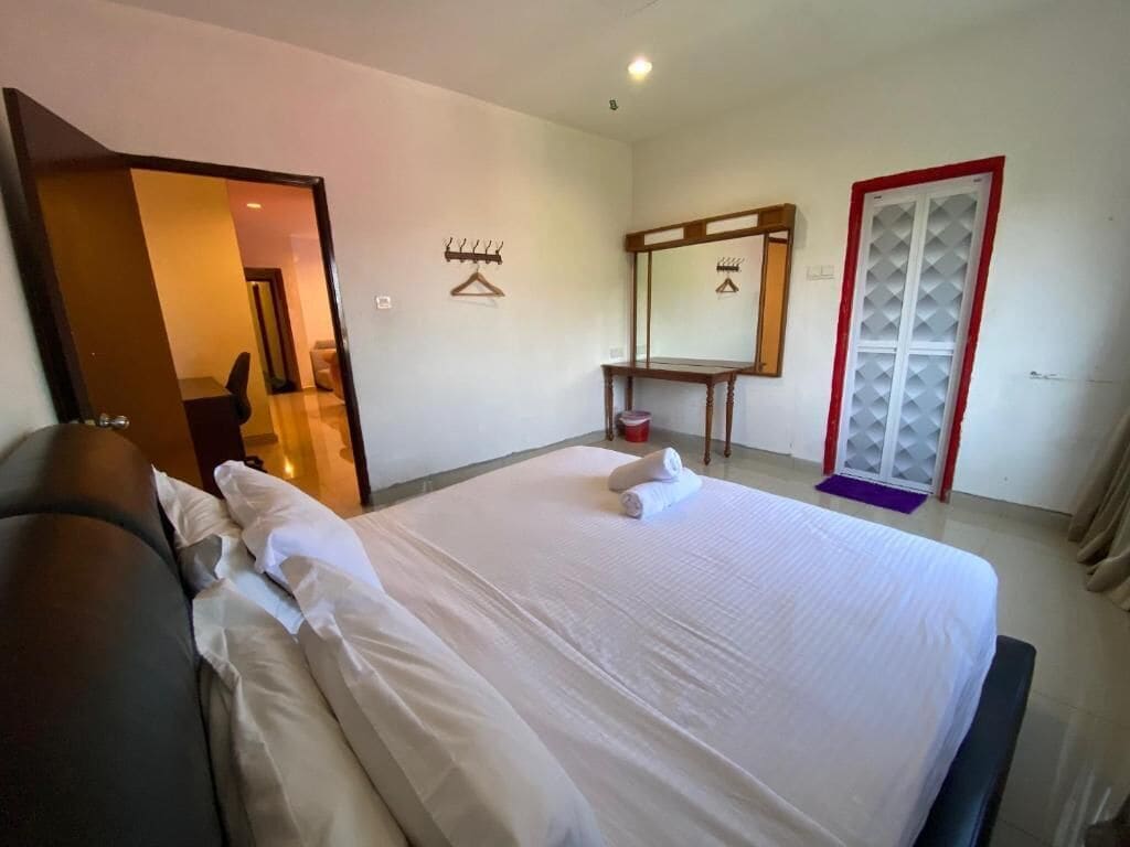 A hotel room with a large bed, a bedside table, a mirror, a wardrobe, and a seating area with a sofa.