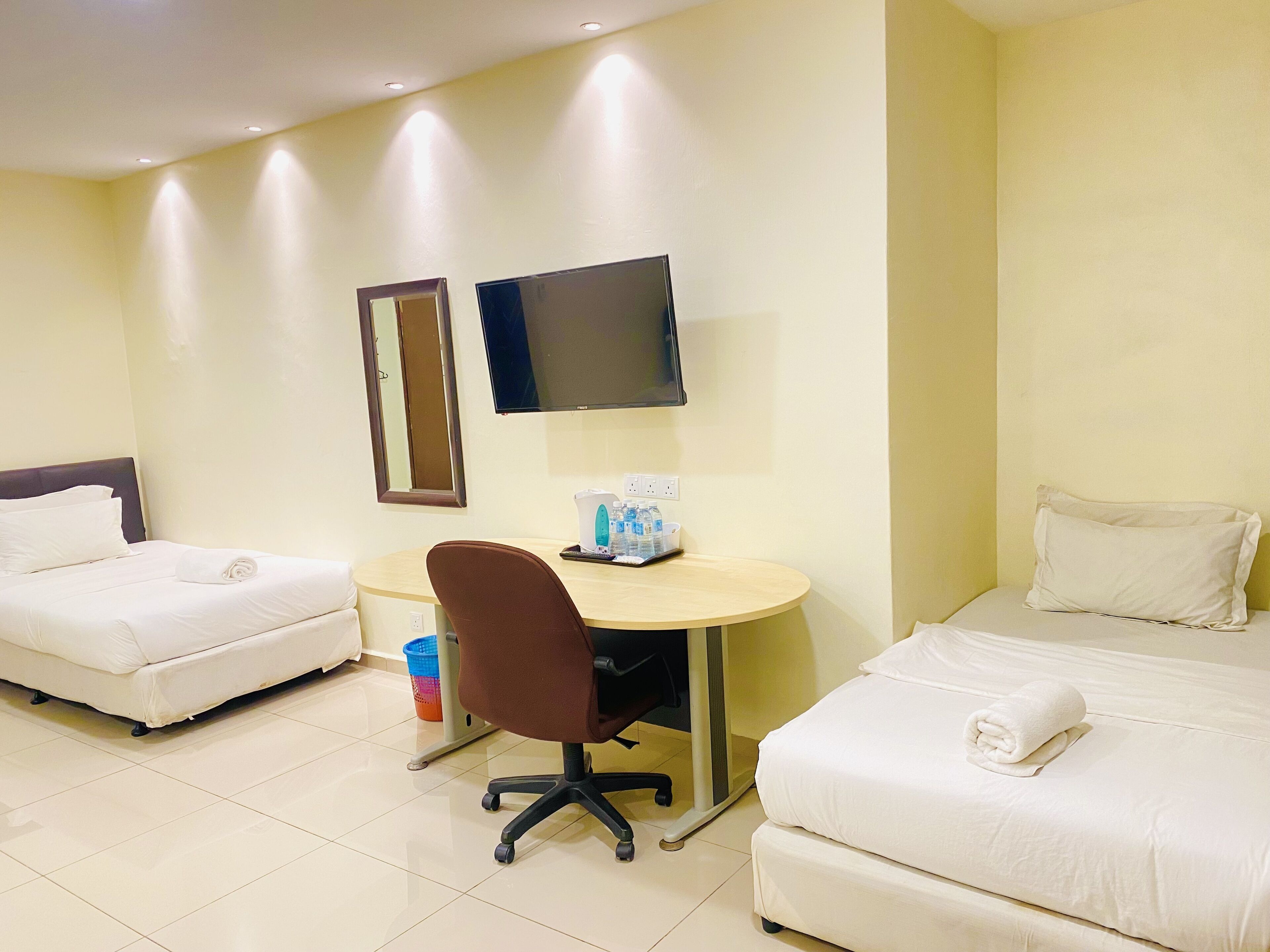 Une chambre d’hôtel avec deux lits, un bureau avec une chaise, un téléviseur à écran plat et un miroir au mur.