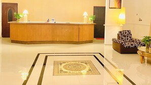 A lobby with a reception desk, a chandelier, a ceiling fan, a patterned rug, and a seating area with a patterned armchair. - Sunsega Hotel (Perai)