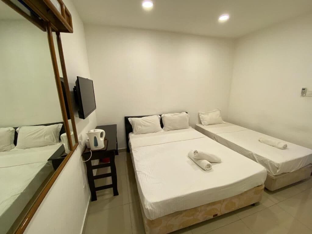 A hotel room with two single beds, a small table with a kettle, a flat-screen TV mounted on the wall, and a wooden chair.