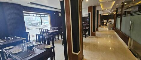 A modern restaurant with marble flooring, dark wooden tables, and a view of the street through large windows.