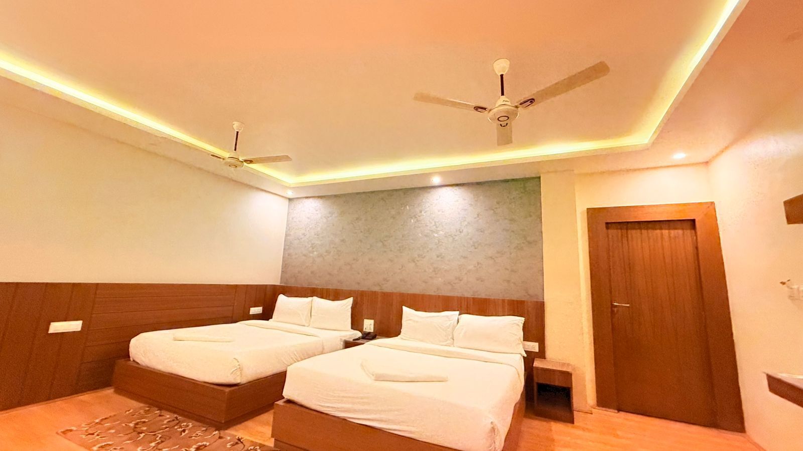 A hotel room with two beds, a ceiling fan, and a wooden door.