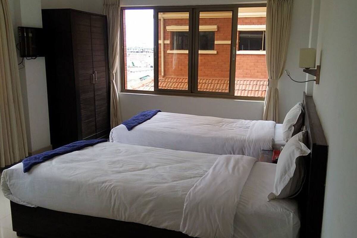 A hotel room with two beds, a wardrobe, a window with curtains, and a wall-mounted TV.