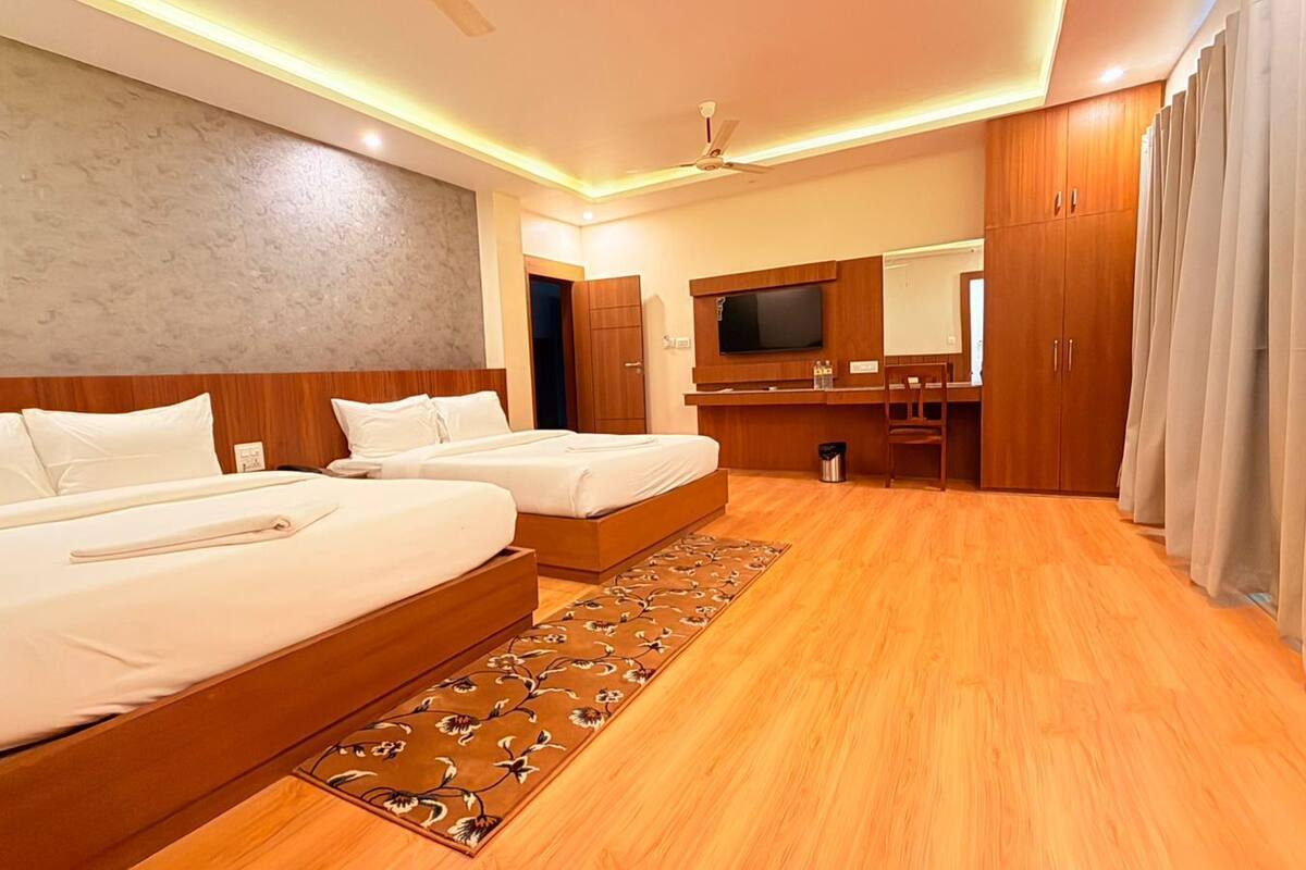 A hotel room with two beds, a wooden floor, a large mirror, and a TV.