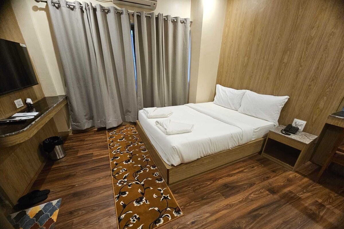 A hotel room with a wooden floor, a bed with white linens, a desk with a telephone, and a window with curtains.
