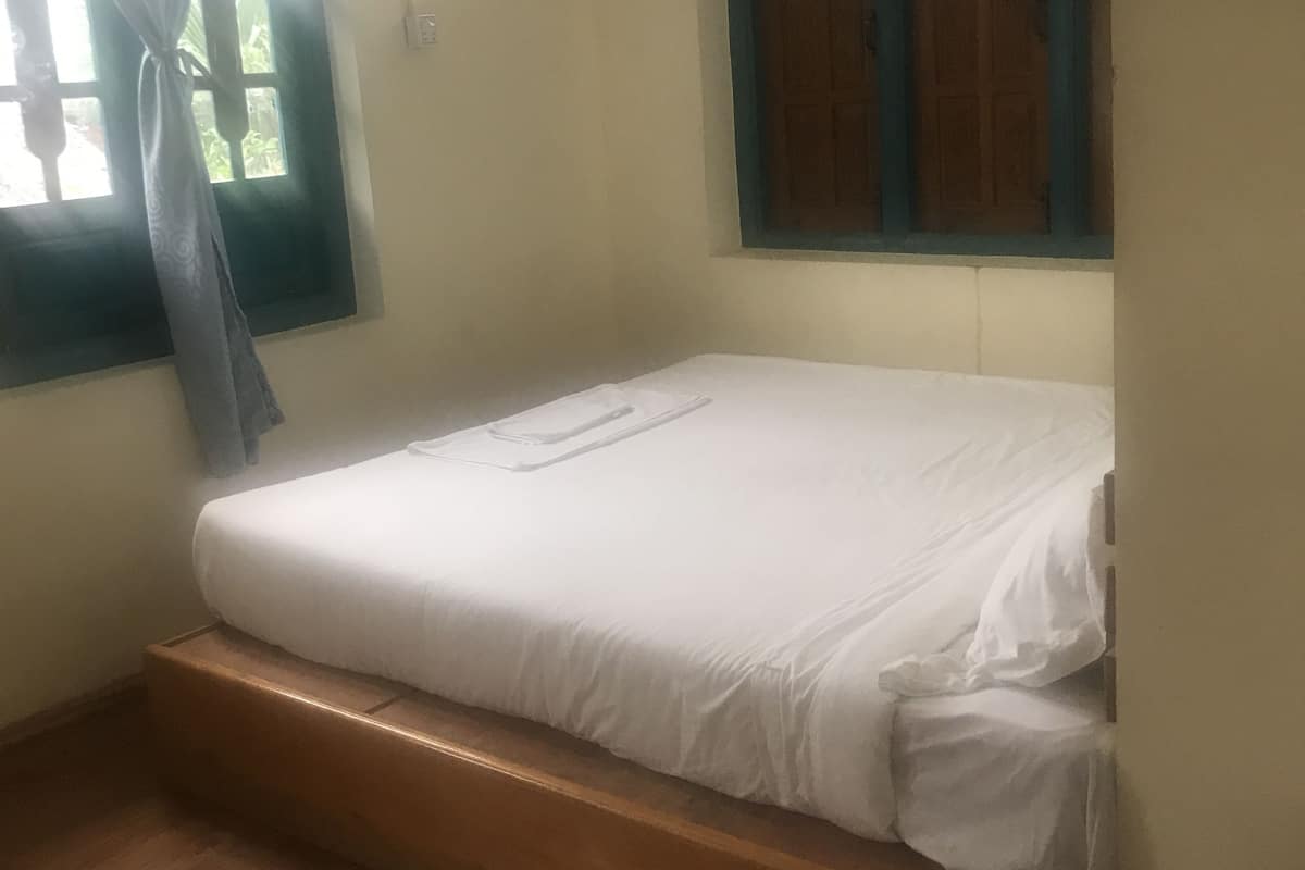 A single bed with a wooden frame, a window with a curtain, and a wooden floor.