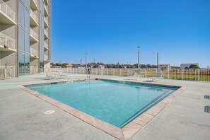 Una piscina rectangular con borde de azulejos, rodeada por una plataforma de hormigón y barandillas blancas.