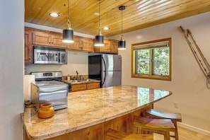 Cocina con armarios de madera, electrodomésticos de acero inoxidable y encimera de granito.