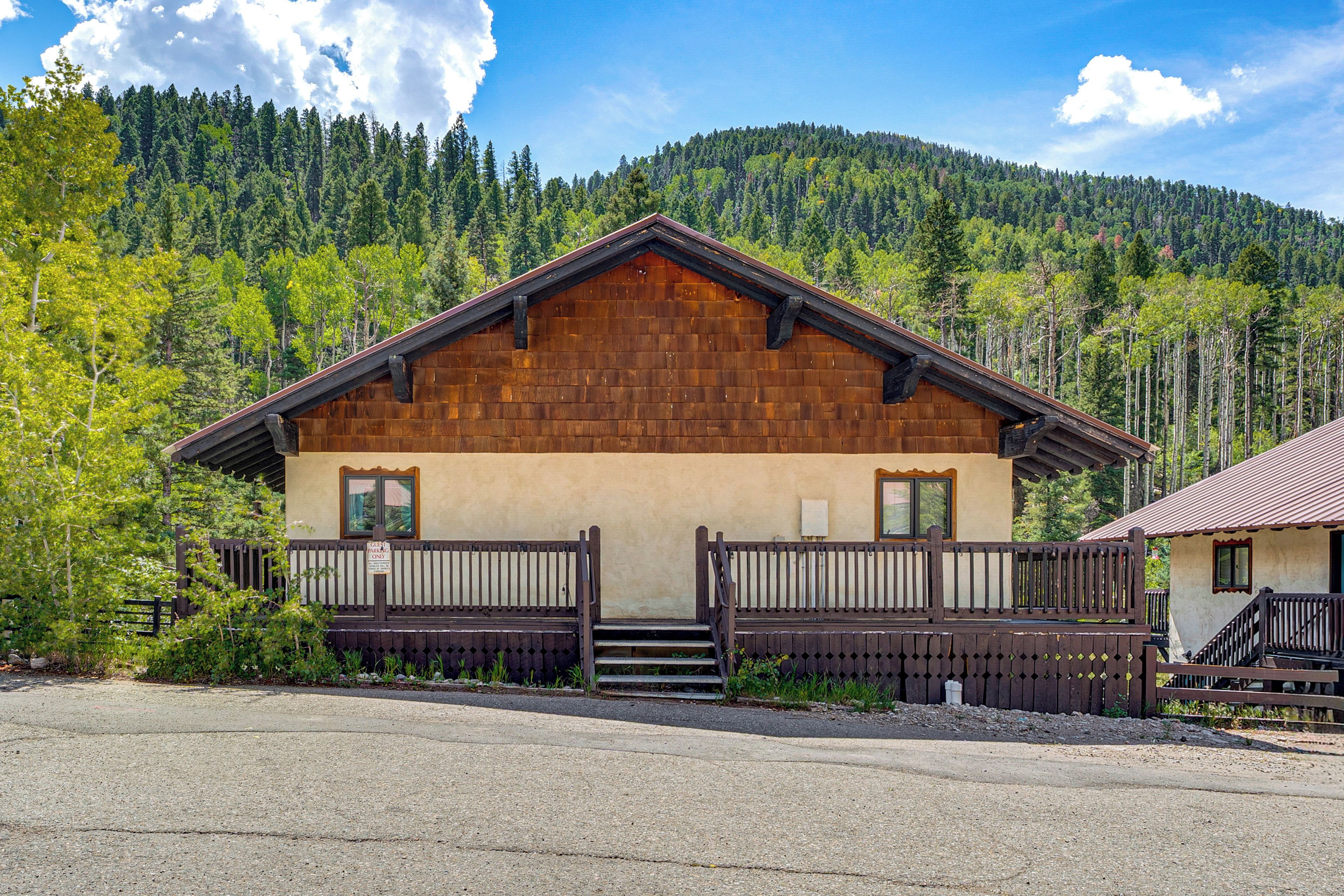 A wooden cabin with a balcony, surrounded by a forested mountain backdrop.