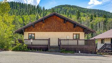 A wooden cabin with a balcony, surrounded by a forested mountain backdrop.